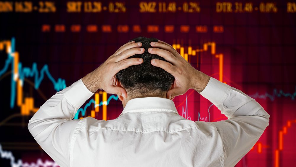 Ein Händler mit dem Kopf in der Hand starrt verzweifelt auf eine digitale Wand mit fallenden Aktienkursen.