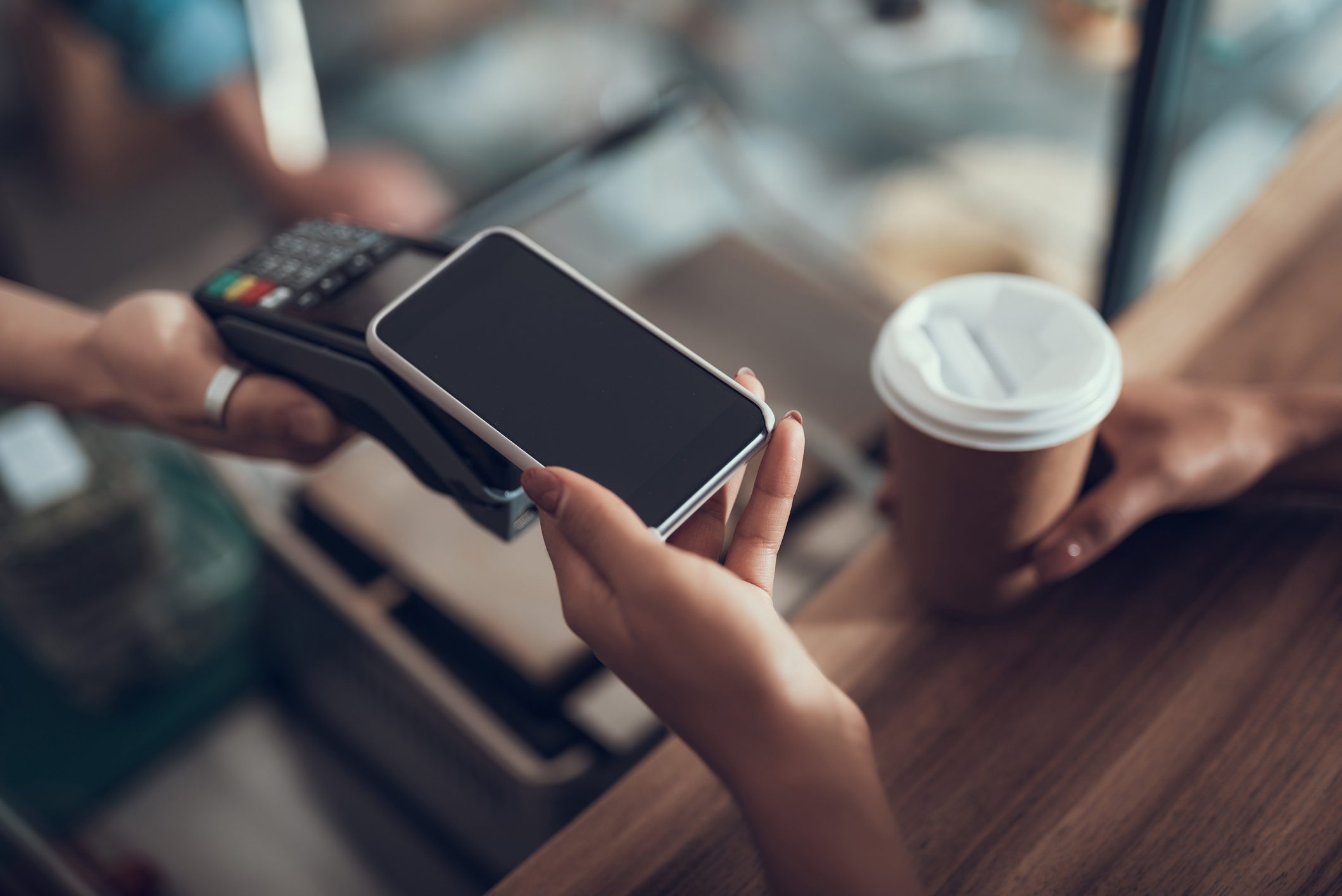 Hand einer jungen Dame, die ihr Smartphone auf einen Kreditkarten-Zahlungsautomaten legt